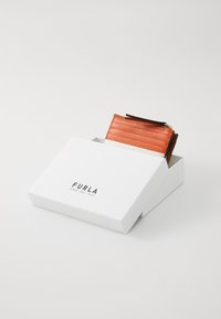 Lærveske i lys orange, med ribbet tekstur og gullglidelås, plassert inni en hvit boks med svart logo.