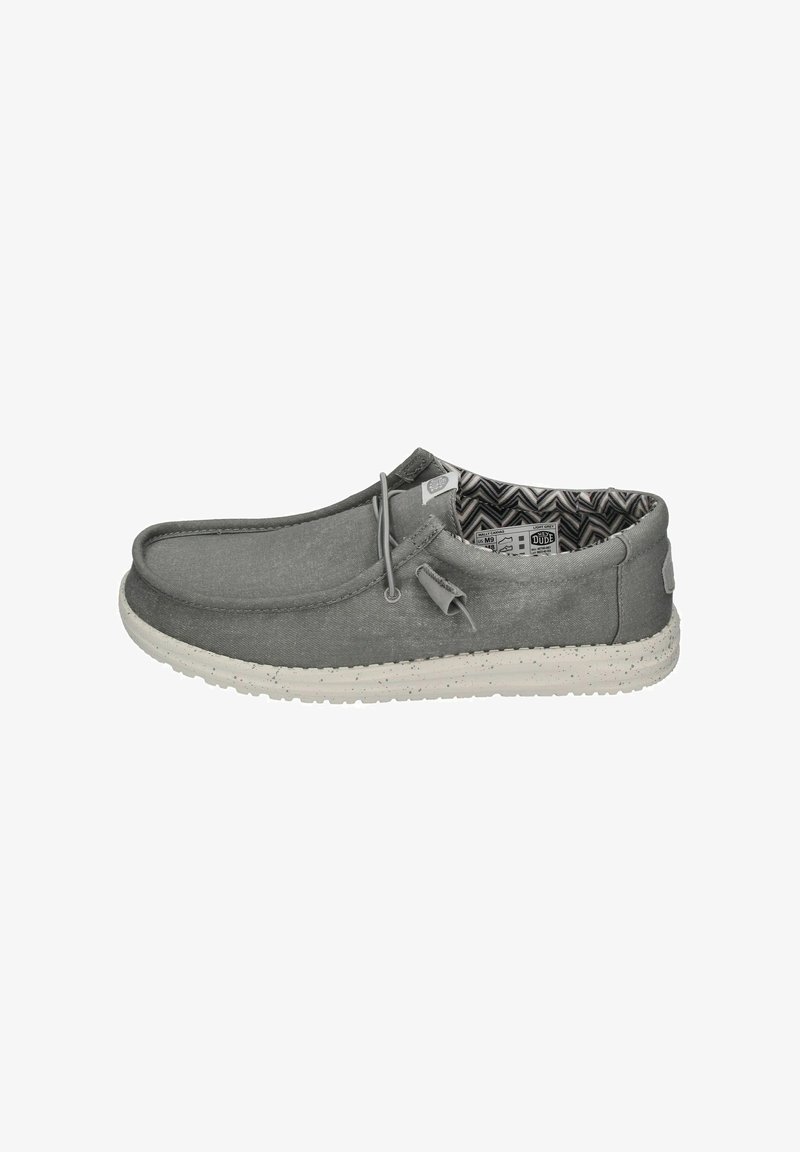 Zapato slip-on de lona gris con una suela de goma texturizada de color claro. El interior tiene un patrón en zigzag. Los cordones realzan el diseño casual.