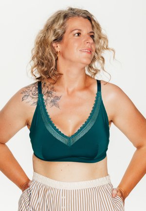 Bralette turchese con bordo in pizzo, design a scollo a V e spalline regolabili. Abbinato a pantaloni corti a vita alta a strisce bianche e beige.