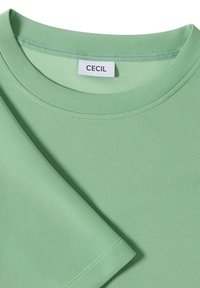 T-shirt à col rond à manches courtes de couleur vert clair, avec l'étiquette de marque visible "CECIL" à l'intérieur du col.