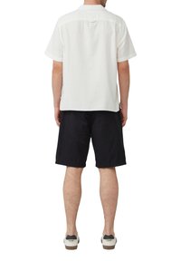 Witte kortearmige shirt met een eenvoudige textuur en een kraag, gecombineerd met zwarte shorts en casual sneakers met een contrasterende hielvoering.