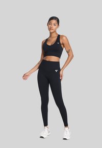 Zwarte sportbeha en high-waisted legging gemaakt van rekbaar materiaal. Heeft een klein logo op de bovenste linkerkant van de beha en op de tailleband.