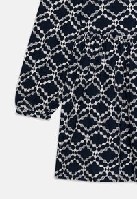 Robe navy avec un motif géométrique blanc. Comprend des manches longues, une taille froncée et un tissu texturé. Les accents incluent des broderies détaillées.