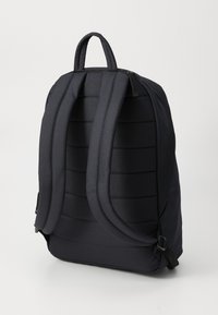 Black padded backpack shown from back with two adjustable straps and a top handle on a white background.