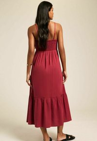 Robe maxi bordeaux avec bretelles réglables, corsage smocké et jupe évasée à volants. Fabriquée en tissu doux, elle présente une coupe décontractée.