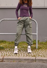 Langärmliges lila Oberteil mit "Levi's California" Grafik, olivgrüne Cargo-Hosen mit Seitentaschen und hellgraue Sneakers mit lila Akzenten.