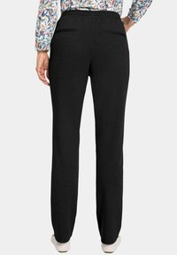 Zwarte, zacht aanvoelende broek met een relaxte pasvorm, voorzien van een elastische tailleband en twee achterzakken. De achterkant toont taps toelopende benen.