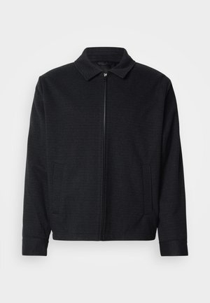 Schwarze Jacke mit strukturiertem Gewebe, Reißverschluss vorne, spitzem Kragen und zwei Seitentaschen. Mit elastischen Bündchen und geradem Saum.