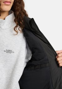 Grauer Sweatshirt mit dem Logo "Element Skateboard Co.". Schwarze Jackeninnenseite zu sehen, mit glatter Textur und Reißverschlussdetails.