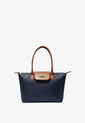 Sac cabas bleu marine avec anses en cuir marron et rabat, fermeture éclair dorée et petite plaque de marque dorée sur le rabat.