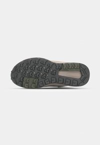Semelle de chaussure de trail avec un motif de crampons en caoutchouc noir robuste, dotée d'accents verts et d'une semelle intermédiaire brun moyen, conçue pour l'adhérence et la durabilité.