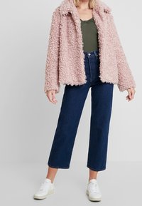 Sametová růžová bunda s límcem, spárovaná s tmavomodrými širokými džínami a bílými teniskami. Texturovaná tkanina a uvolněný střih.