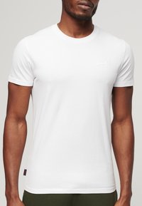 Short-sleeve white t-shirt made of cotton with a crew neckline; features a small embossed logo on the chest and textured fabric.