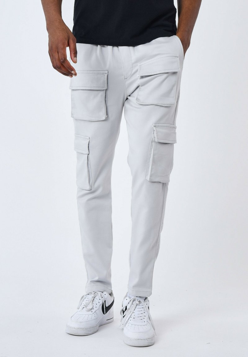 Pantalones cargo de color gris claro con múltiples bolsillos, diseño ajustado y una textura suave, combinados con zapatillas blancas con acentos negros.