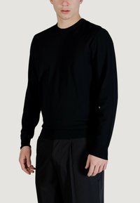 Maglione nero a maniche lunghe con collo tondo, realizzato in materiale morbido. Presenta orlo e polsini a coste, abbinato a pantaloni scuri e sartoriali.