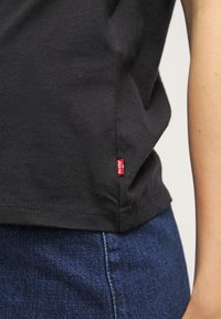Svart bomullströja med korta ärmar, med en liten röd Levi's-logotyp på sidan av sömmen. Texturerat tyg och rak fåll.