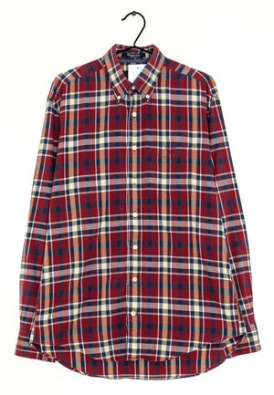 Chemise à manches longues boutonnée avec un motif à carreaux rouge, bleu marine, blanc et jaune, suspendue sur un cintre noir.