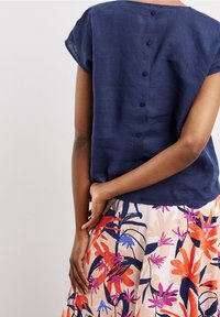 Haut en lin bleu marine à manches courtes avec bouton au dos, associé à une jupe à motif floral aux teintes orange, rose et bleues.