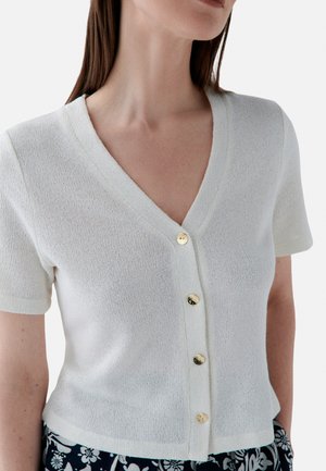 Cardigan en tricot blanc à manches courtes, décolleté en V profond et cinq boutons dorés sur le devant ; texture légère avec un léger éclat.