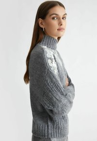 Maglione grigio a maglia con colletto alto a costine, maniche testurizzate e dettagli in paillettes sulle spalle. Design morbido e voluminoso.