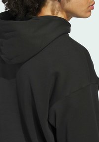 Felpa nera con cappuccio caratterizzata da una vestibilità comoda, tessuto testurizzato e un grande cappuccio. Cuciture visibili e leggera drappeggiatura nel tessuto.