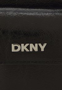 Melnā mākslīgās ādas maka, kas izceļas ar metāliski sudraba "DKNY" logo. Materiāls ir ar teksturētu virsmu, kurā redzami raksti.