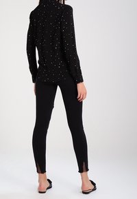 Camiseta negra de manga larga con un patrón de puntos, combinada con leggins negros ajustados que presentan detalles de encaje en los tobillos.