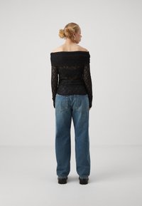Top off-shoulder in pizzo nero con maniche lunghe, abbinato a jeans in denim blu larghi e scarpe platform nere spesse, visto da dietro.