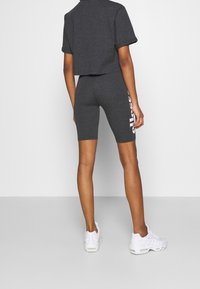 Szara krótka koszulka i dopasowane szorty rowerowe, z logo po boku. Materiał wydaje się miękki, o gładkiej fakturze. Białe trampki.