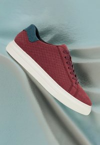 Bordeaux sneaker met een gewatteerde textuur, witte zool en blauwe accenten bij de hak. Voorzien van ronde veters en strakke, rechte lijnen.