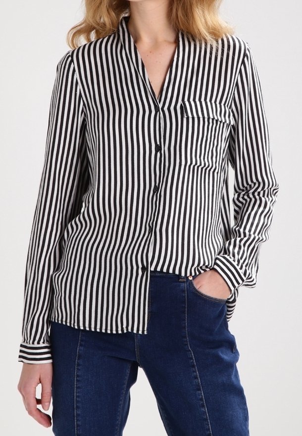 Camisa de manga larga a rayas blancas y negras con cierre de botones, cuello y bolsillo. Se lleva con vaqueros azul oscuro. Textura de tela lisa.