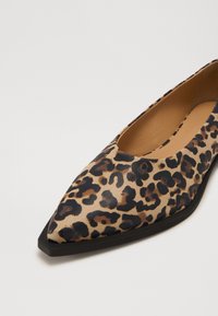 Zapato plano de estampado de leopardo con puntera afilada, hecho de cuero suave. Presenta una suela negra y acentos en patrón beige y marrón.