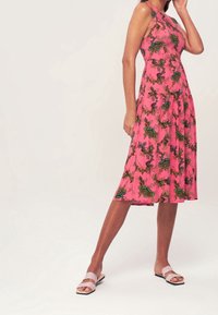 Rosa ärmelloses Kleid mit floralem Muster in Grün und Gold, ausgestellter Rockdesign, kombiniert mit hellrosa Sandalen mit zwei Riemen.