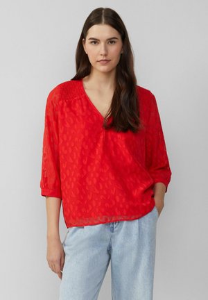 Blouse en voile rouge avec un décolleté en V et des détails smockés sur les épaules. Présente un motif léopard subtil et des manches trois-quarts.