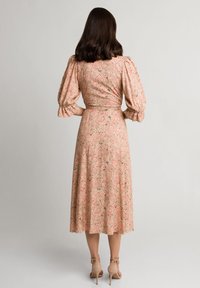 Sukienka midi w kwiatowy wzór w kolorze brzoskwiniowym, z bufkami, dopasowaną talią i zwiewnym dołem. Noszona z cielistymi szpilkami.