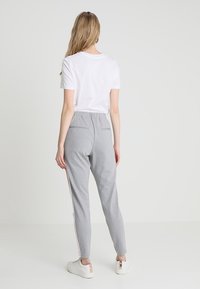 Grå sweatpants med en tajt passform, elastisk midjeband och två bakfickor. Har vertikala rosa sidosträck. Kombineras med en vit T-shirt.