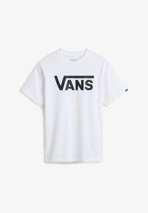 Camiseta blanca de manga corta con el logo negro de "VANS", combinada con pantalones marrones y un suéter azul atado a la cintura, completando el look con zapatillas azules.