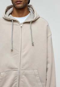 Lichtbeige zip-up hoodie met een trekkoordcapuchon, voorzakken en textielstof. Beschikt over een ontspannen pasvorm en zichtbare stikseldetails.