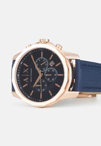 Orologio in oro rosa con cassa ottagonale, quadrante nero, tre sottodial e cinturino in pelle blu navy testurizzato. Include display della data alle 3.