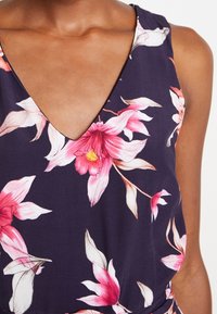 Robe à fleurs avec un décolleté en V profond, fond bleu marine et motifs floraux roses. Fabriquée en tissu léger à texture douce.