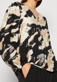 Langærmet bluse med V-hals lavet af letvægtsstof med et sort, beige og hvidt abstrakt mønster; har samlede manchetter og knapdetalje.