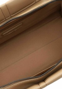 Intérieur d'un sac à main en cuir tan avec une texture lisse, fermeture zippée et design minimaliste. Doublé d'un tissu beige clair.