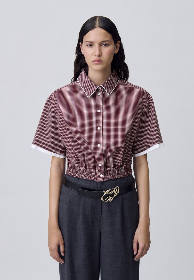 Blusa de manga corta a cuadros en burdeos y blanco, que presenta un alto cuello, cintura elástica y puños blancos a contraste con botones.