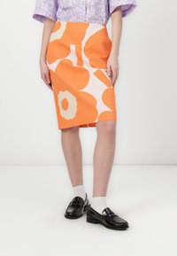 Jupe florale orange avec de grands motifs pêche et crème. La jupe est droite et arrive au genou, faite d'un tissu structuré.