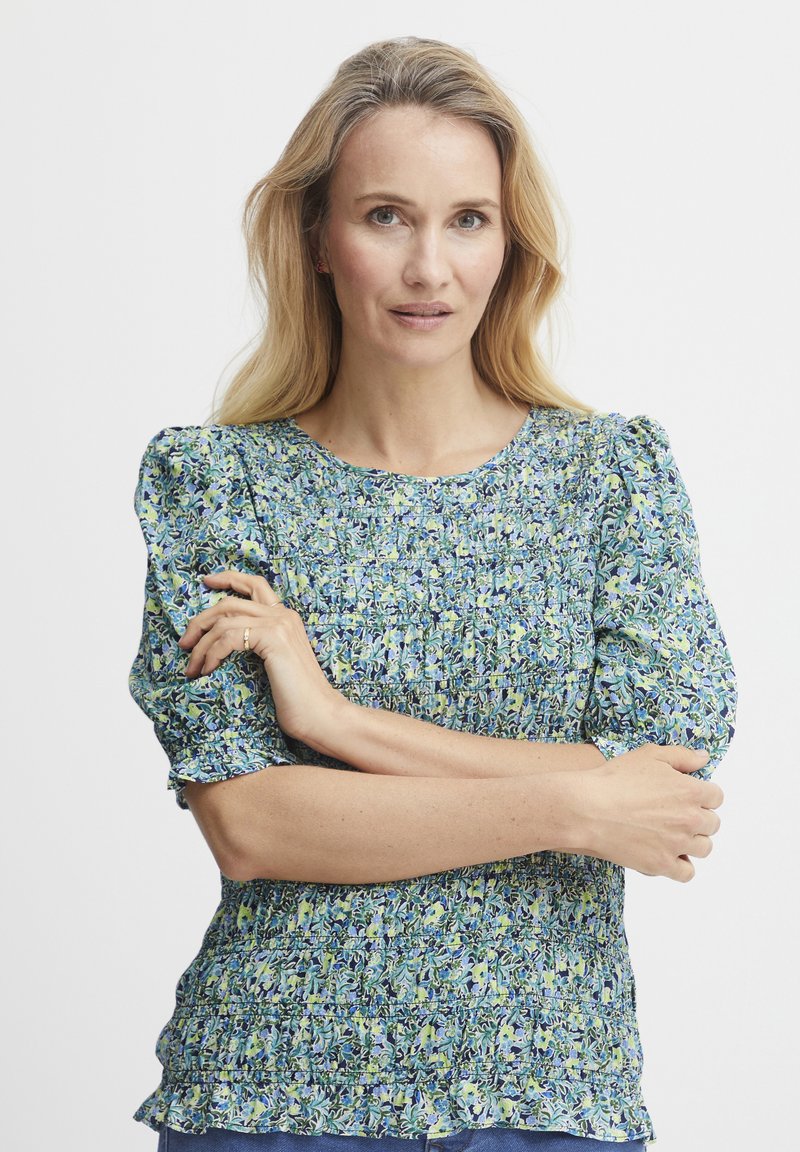Bluză cu model floral, cu mâneci scurte tip puff, textură smock și gât rotund, în nuanțe de albastru, verde și galben.
