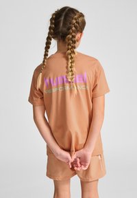 Brun t-shirt med korte ærmer og en rund kant, der har stor lilla og turkise "hummel PERFORMANCE" tekst på ryggen.