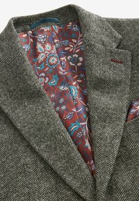 Blazer en chevrons gris avec une doublure floral bordeaux et un pochette. Tissu texturé avec des accents contrastants.