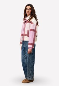 Roze en crèmekleurige oversized jas met gestreept patroon, voorzien van een kraag en knoopsluiting, gecombineerd met donkerblauwe baggy jeans en beige schoeisel.