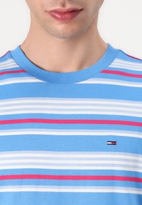 Camiseta a rayas en azul claro con rayas horizontales en blanco y rosa. Cuello redondo y pequeño logo bordado en el pecho.