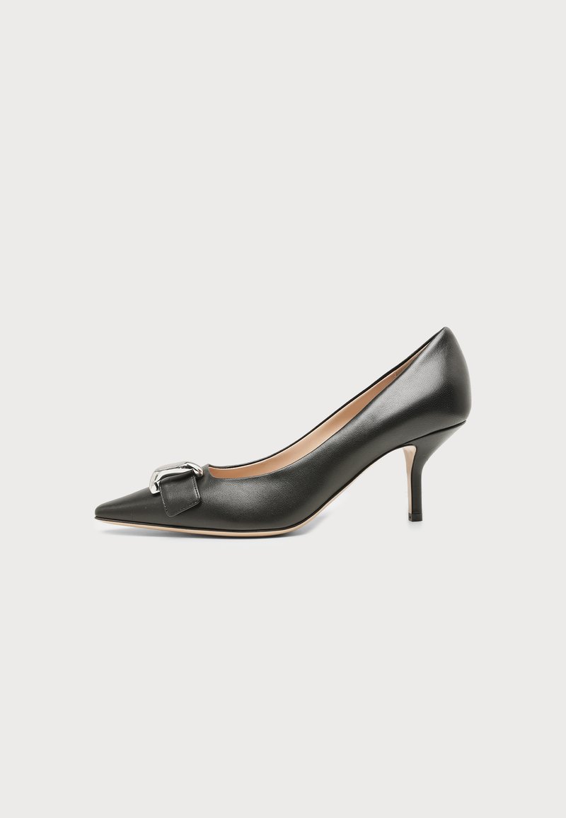 Chaussure à talon haut en cuir noir à bout pointu avec talon aiguille de hauteur moyenne et détail de boucle argentée à l’avant, présentée sur fond clair uni.